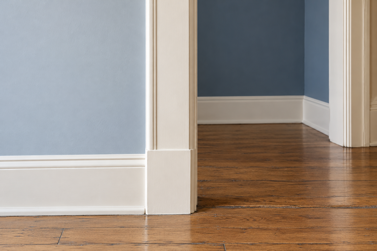 A close view of a warm white door casing, with pale blue gray hall wall on one side and slate blue living room wall on the other, each stopping cleanly at the casing's edge.