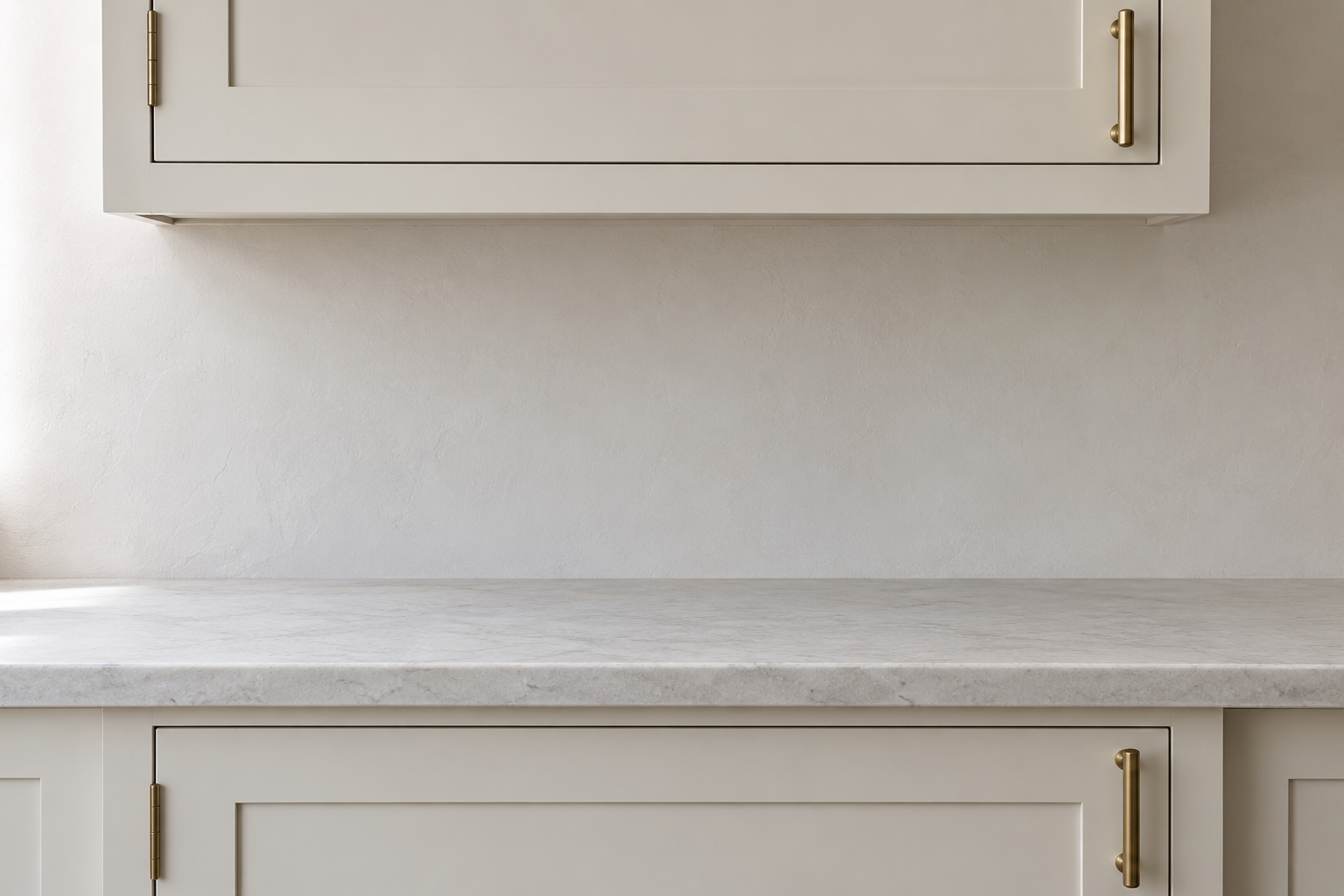 A wall cabinet door with a vertical brass pull at its bottom corner above a base cabinet door with a pull at its top corner.