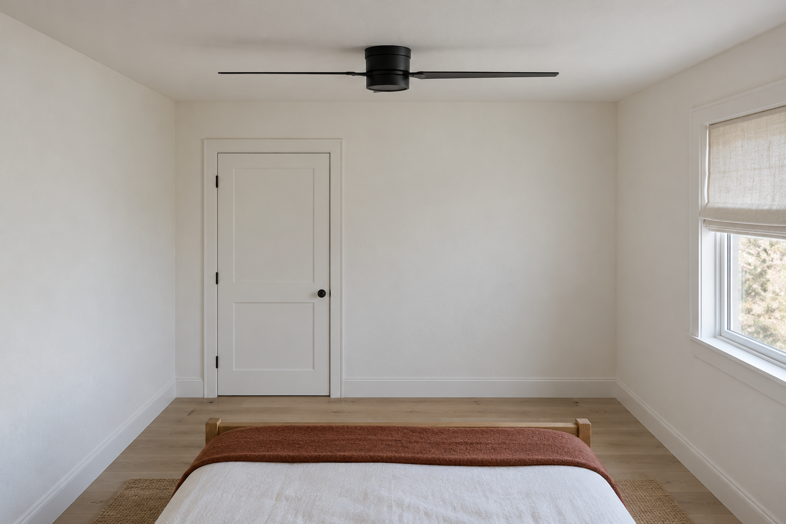 A compact black ceiling fan fixed flush to the low ceiling of a white bedroom, its blades just above the height of the top of the door frame.