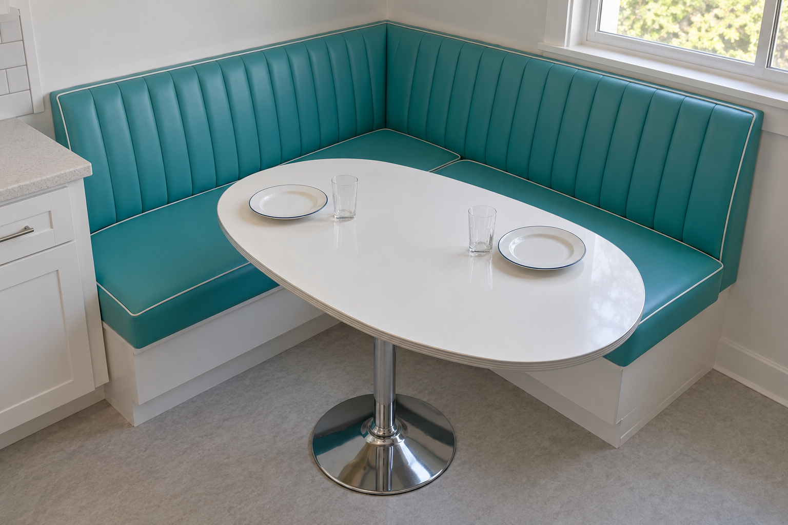 The inside corner of an L-shaped turquoise banquette with an oval pedestal table and two place settings.