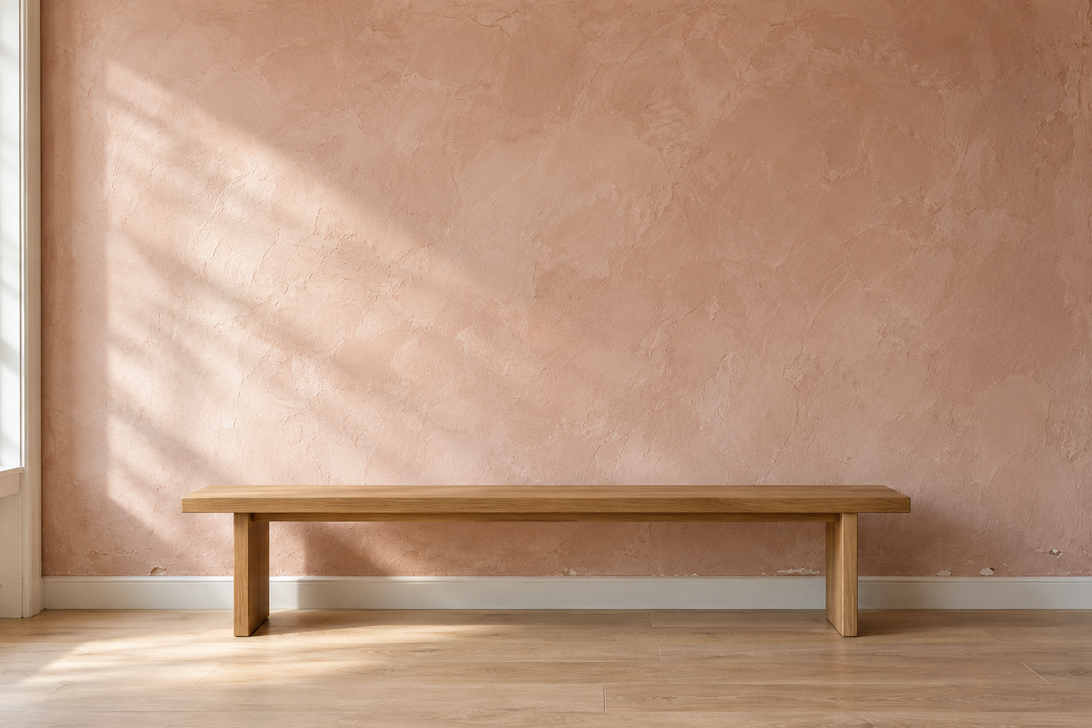 A wall finished in pale pink clay plaster with soft cloudy movement, lit by raking daylight, behind a low oak bench.
