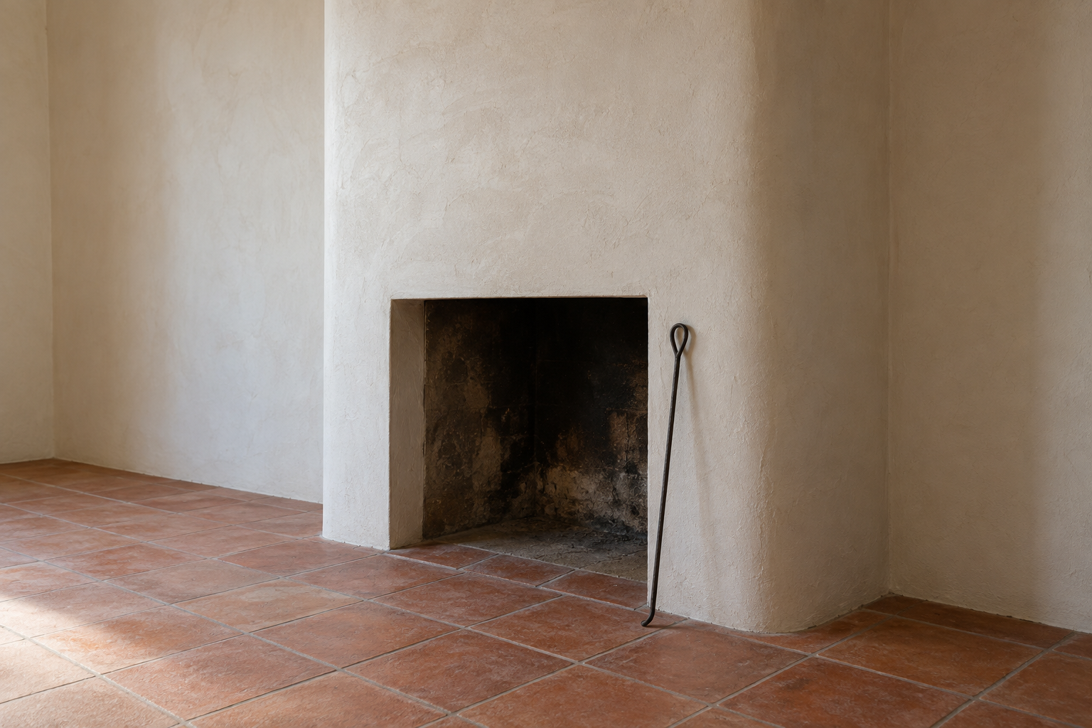 A smooth ivory plaster chimney breast with rounded corners and no mantel, beside a terracotta tile hearth.