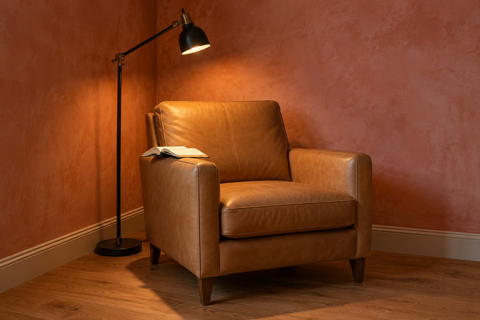 An empty tan leather reading chair with a black adjustable floor lamp behind and to one side of it, its small shade angled down over the chair's arm onto an open book.