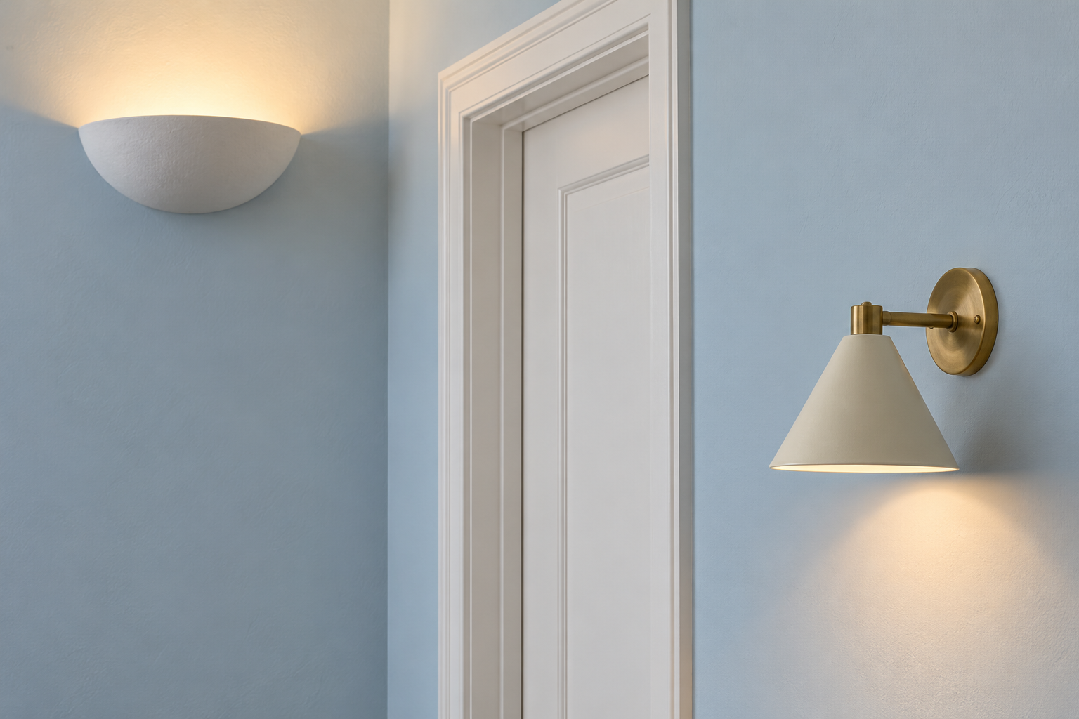 Two wall lights on a pale blue wall: a plaster bowl uplight mounted high and a brass sconce with a downward cone shade mounted lower.