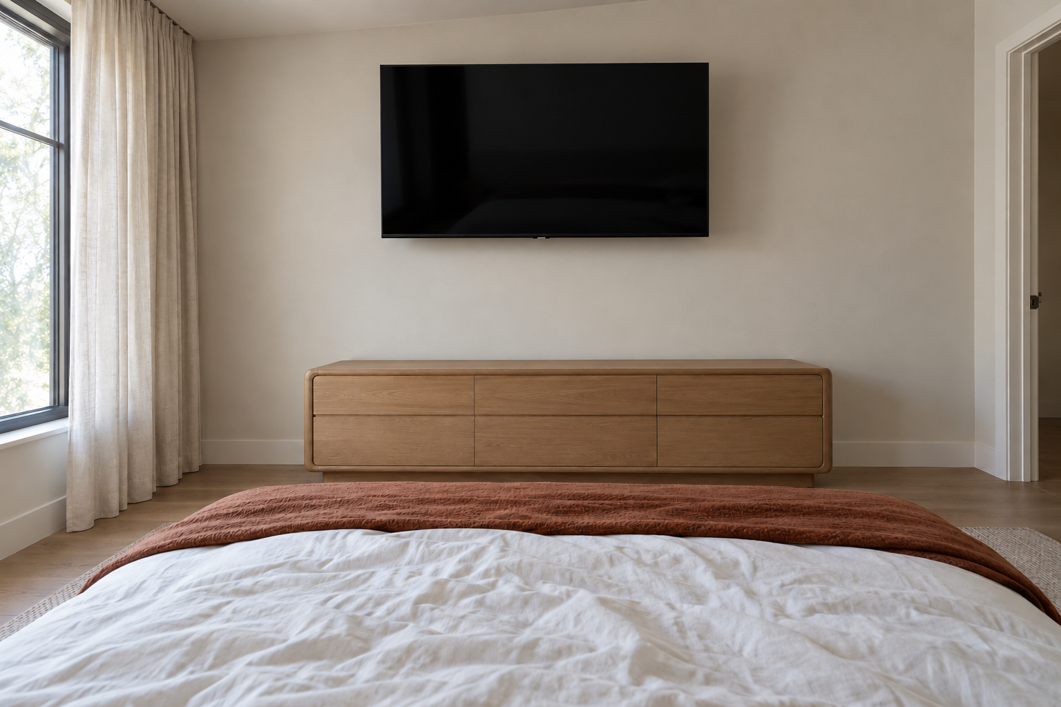 A television mounted high on a bedroom wall above a low oak dresser, seen from the pillows.