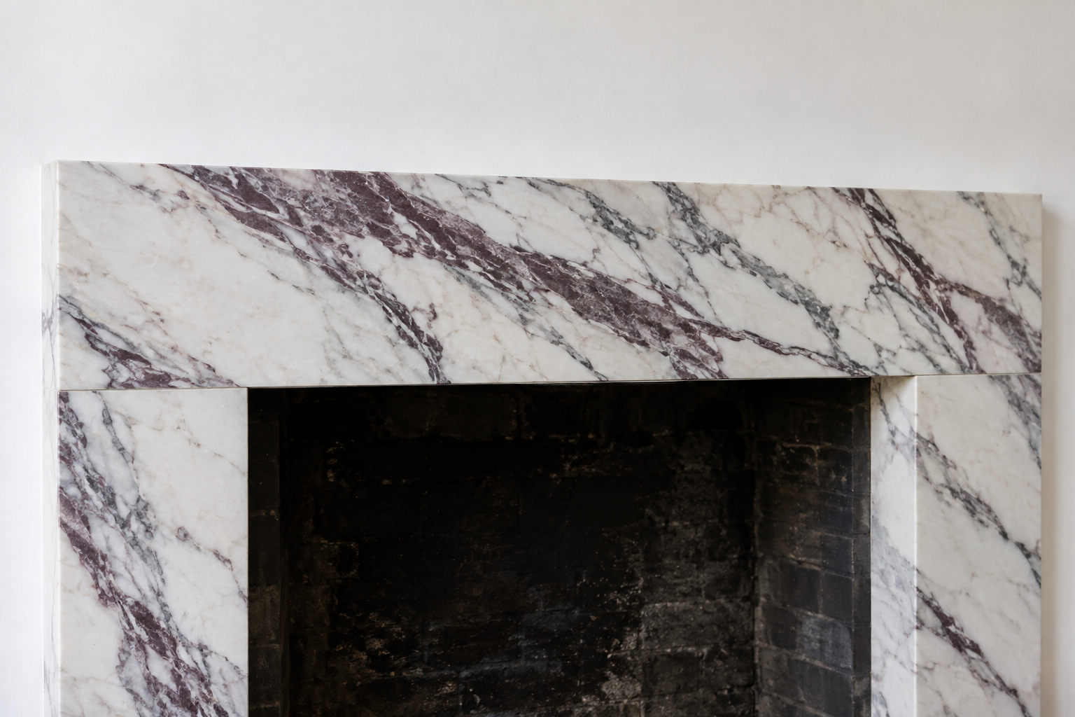 A plain fireplace surround in white marble with strong plum and gray veining running across the header.