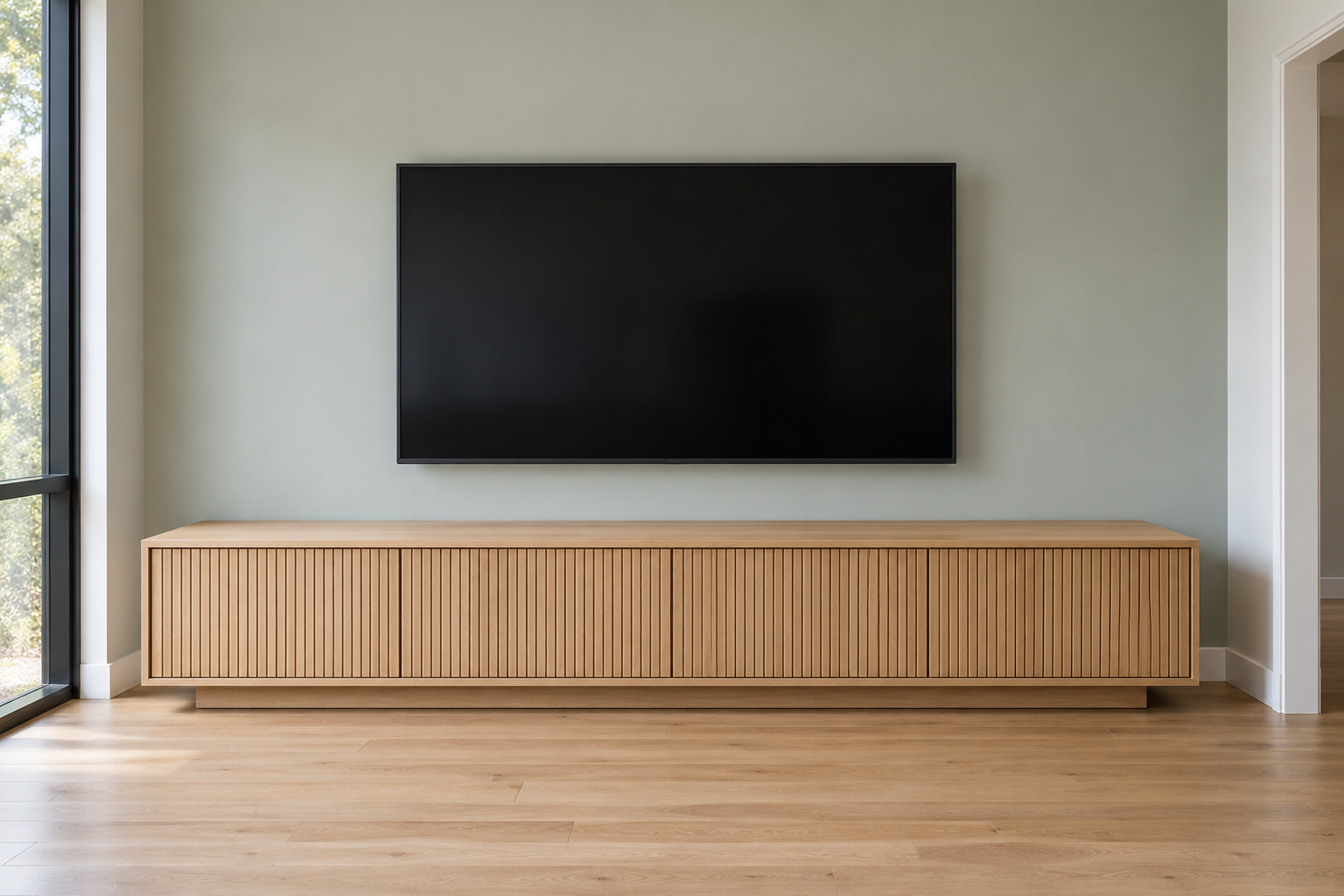A long, low oak media console with closed slatted doors under a wall-mounted TV with a dark screen, against a pale gray-green wall.