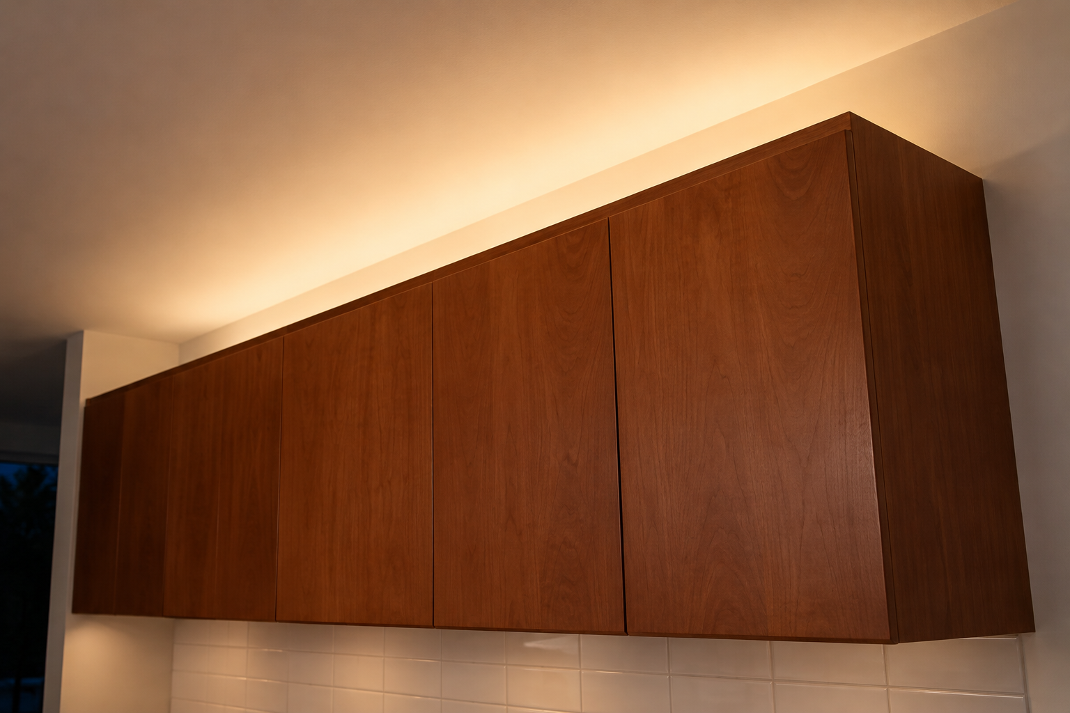 Natural cherry wall cabinets that stop short of the ceiling, with a hidden light on top washing the white ceiling above them.