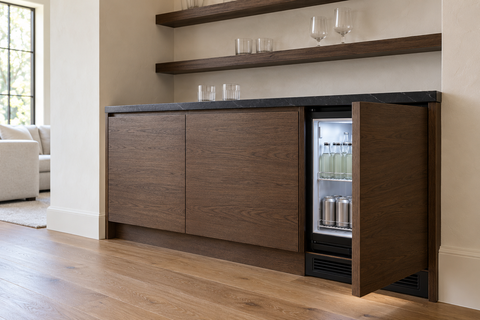 A fumed oak bar run with a black stone counter, where one lower door is the front of a small fridge, slightly open to show bottles inside, with a slim vent grille below it.
