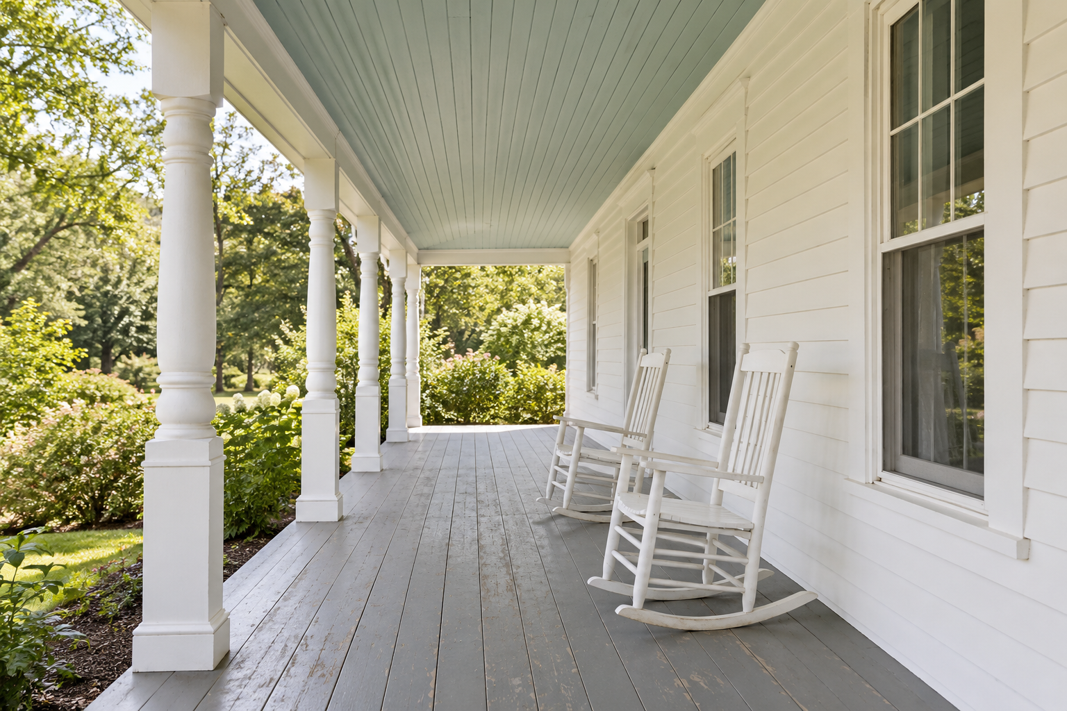 A covered front porch with its board ceiling painted a pale blue-green, white columns, and two rocking chairs.