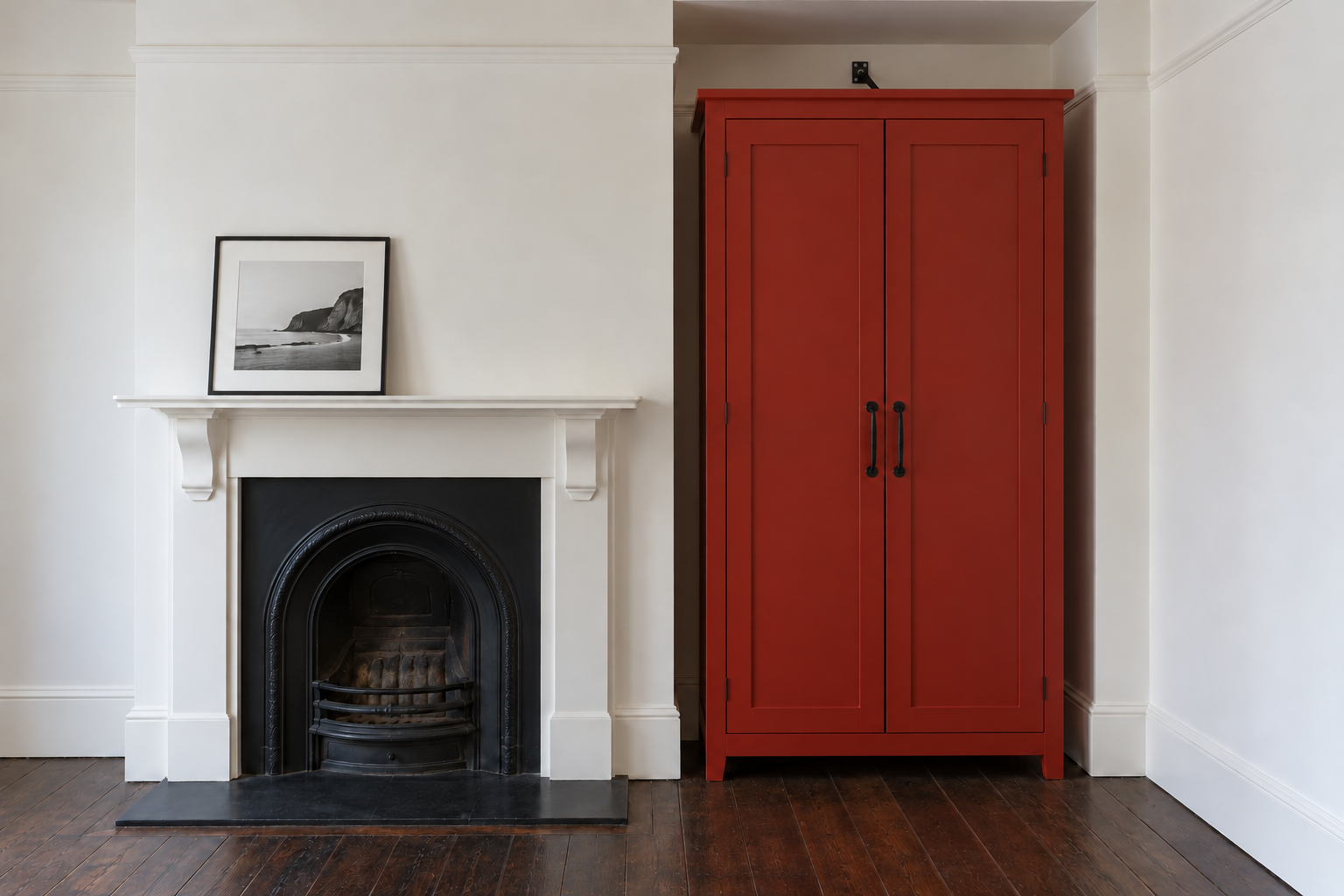 A tall tomato-red cabinet filling an alcove beside a white chimney breast in an older apartment.